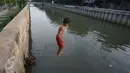 Seorang anak melompat ke anak Kali Ciliwung di Jakarta, Rabu (13/7). Bersihnya kali yang berada di Ibu Kota itu dimanfaatkan anak-anak sekitar untuk berenang sambil mengisi waktu libur sekolah. (Liputan6.com/Immanuel Antonius)