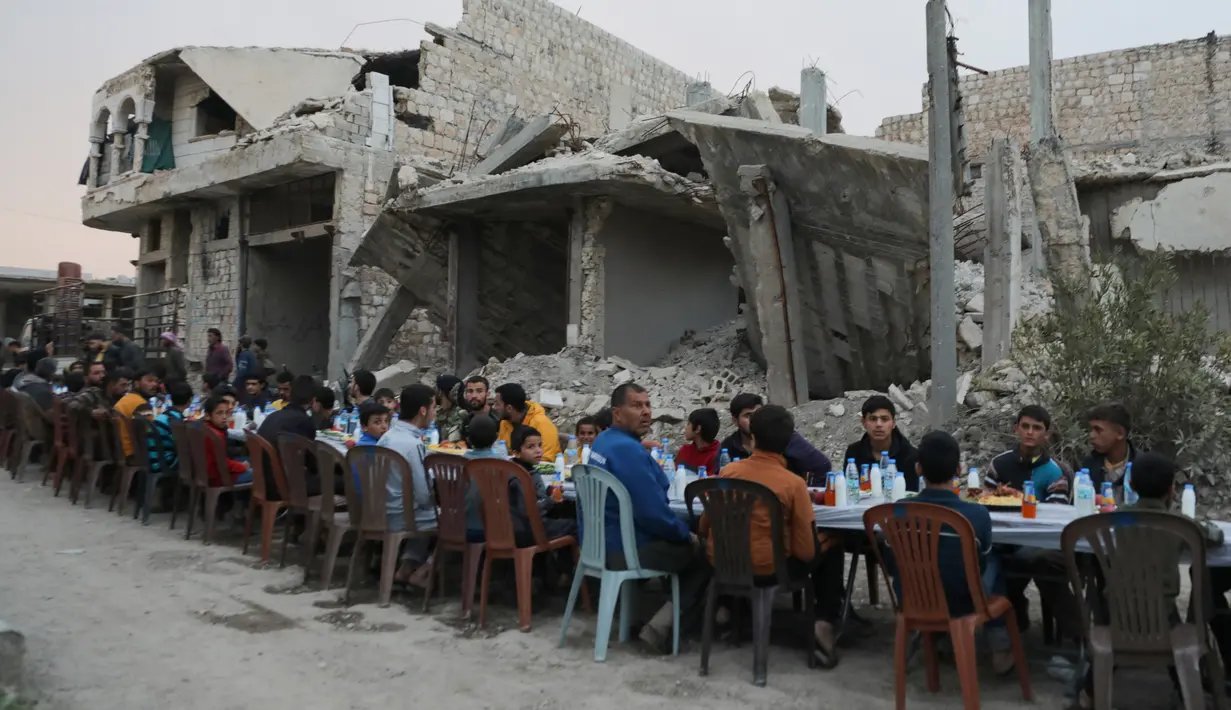 Warga Suriah berkumpul di daerah yang rusak berat untuk berbuka puasa di Tadef, dekat kota perbatasan al-Bab, yang dikendalikan pemberontak yang didukung Turki di Suriah (18/4/2022). Buka puasa ini diselenggarakan oleh sebuah LSM berkoordinasi dengan berbagai faksi lokal. (AFP/Bakr Alkasem)