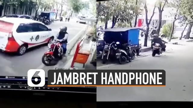 Video CCTV memperlihatkan seorang pria menggunakan sepeda motor menjambret handphone di pinggir jalan.