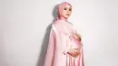 Maternity shoot yang dilakukan Lesty Kejora juga sempat mencuri perhatian banyak orang. Seperti tampilannya di sini yang memakai dress dan hijab satin bernuansa merah muda. Dress polos ini diberi detail bahan organza di bagian dada dan memanjang menjadi cape. Foto: Instagram.