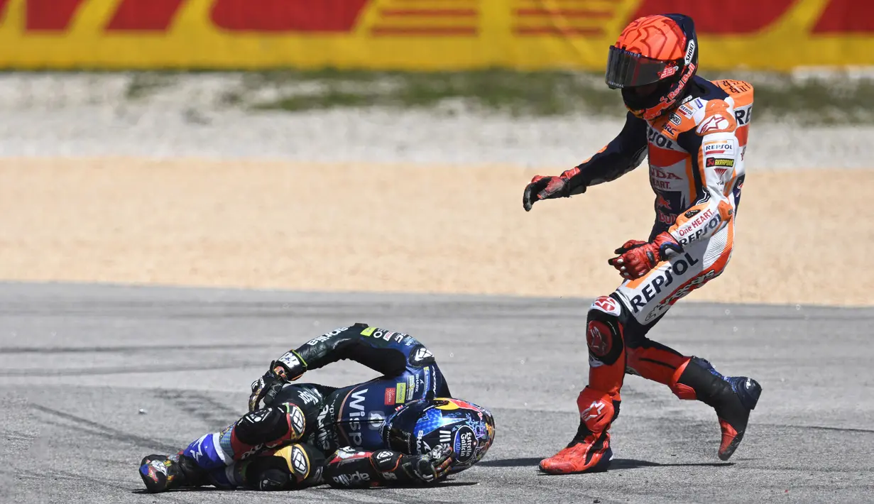 Pembalap Honda, Marc Marquez (kanan), berusaha menolong pembalap Aprilia, Miguel Oliveira, setelah keduanya terlibat kecelakaan dalam MotoGP Portugal 2023 yang berlangsung di Algarve International Circuit, Portimao, Minggu (26/3/2023). (AFP/Patricia De Melo Moreira)