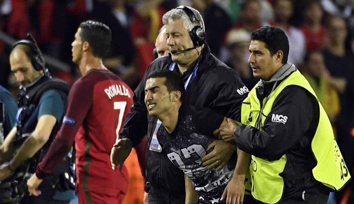 7. Petugas berupaya mengamankan seorang suporter yang masuk ke lapangan untuk mengejar bintang Portugal, Cristiano Ronaldo. Fans ini masuk ke lapangan untuk memeluk dan melakukan selfie dengan Cristiano Ronaldo. (AFP/Lionel Bonaventure)
