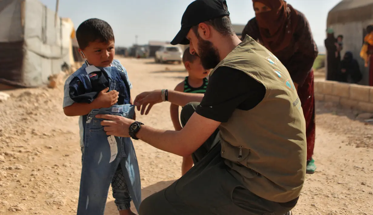 <p>Seorang sukarelawan membagikan pakaian kepada anak-anak Suriah di sebuah kamp di pinggiran kota Dana yang dikuasai pemberontak, di sebelah timur perbatasan Turki-Suriah di provinsi barat laut Idlib (30/4/2022). Umat Islam seluruh dunia bersiap untuk merayakan Idul Fitri yang menandai akhir bulan puasa Ramadhan. (AFP/Aaref Watad)</p>
