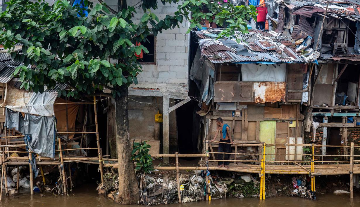 Kepadatan yang sangat tinggi ini disebabkan oleh faktor urbanisasi yang terus meningkat, menjadikan Jakarta sebagai pusat ekonomi dan bisnis nasional. Tampak dalam foto, seorang pria berdiri di atas jembatan bambu yang menghubungkan rumah-rumah di permukiman kumuh tepi sungai yang padat penduduk di Jakarta pada Selasa 21 April 2026. (BAY ISMOYO/AFP)