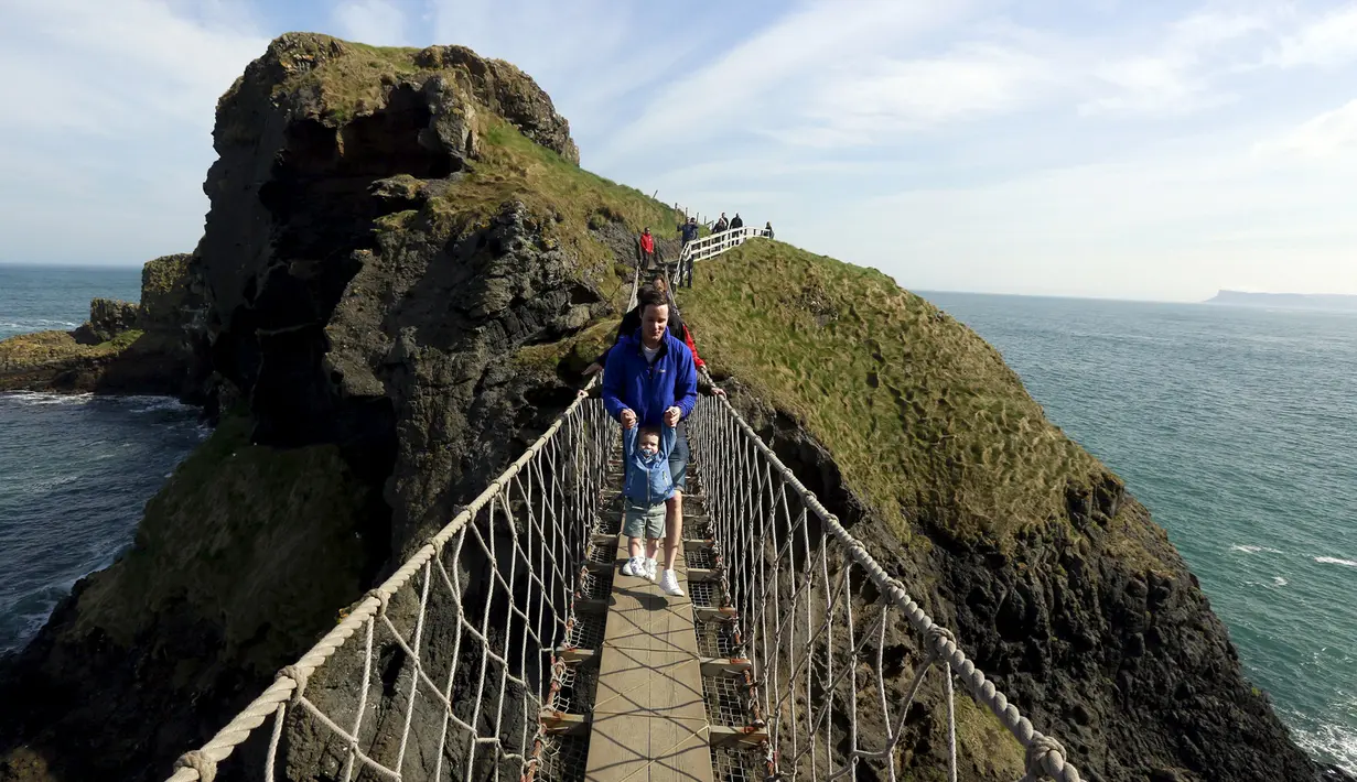 Seorang turis bersama anaknya melintasi Jembatan Carrick-a-Rede Rope di Pantai Causeway, Irlandia Utara, Rabu (8/4/2015). Jembatan tersebut diperkirakan telah dibangun selama lebih dari 350 tahun oleh para nelayan salmon. (REUTERS/Cathal McNaughton) 