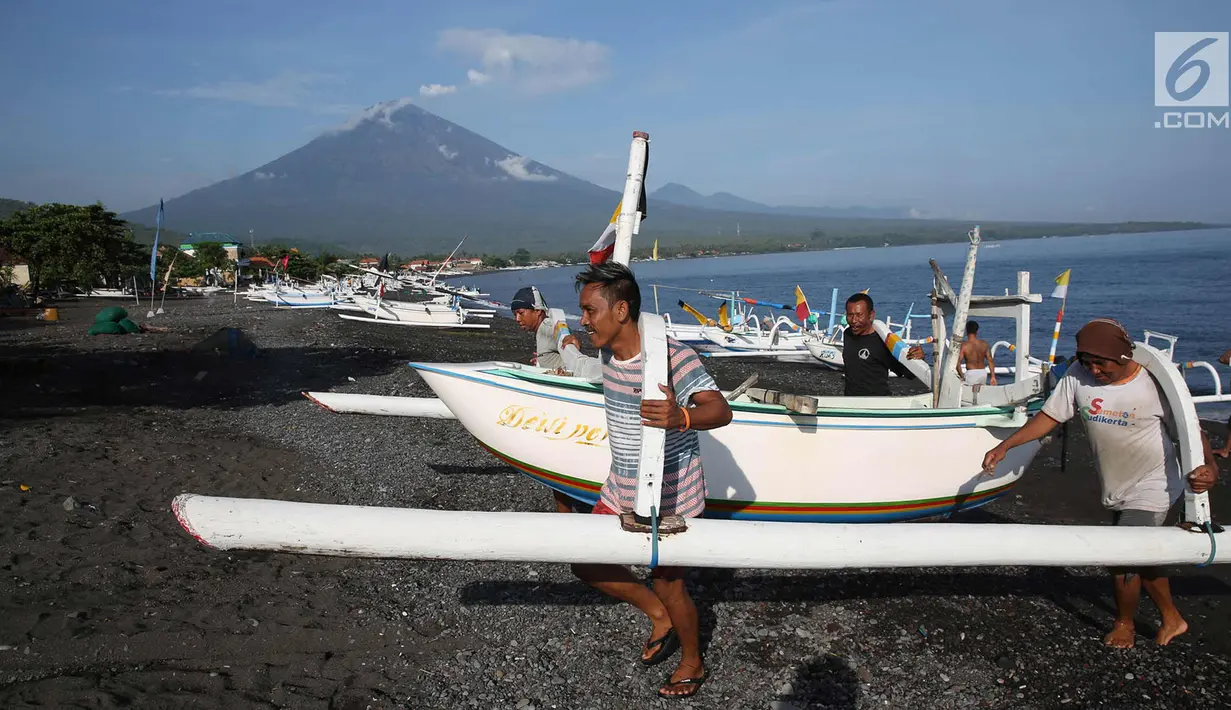 Nelayan mengangkat perahu dengan latar Gunung Agung yang mengeluarkan asap tebal dari kawasan Amed, Karangasem, Bali, Kamis (7/12). Sepekan terakhir, aktivitas Gunung Agung mulai tampak tenang, meskipun masih status Awas. (Liputan6.com/Immanuel Antonius)