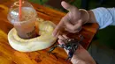 Foto pada 18 Agustus 2018 menunjukkan pelanggan bermain dengan ular piton dan kalajengking di Reptile Cafe, Phnom Penh, Kamboja. Sejauh ini bisnis kafe reptil itu masih berjalan merangkak karena rasa takut umum akan ular dan kadal. (AFP/TANG CHHIN Sothy)