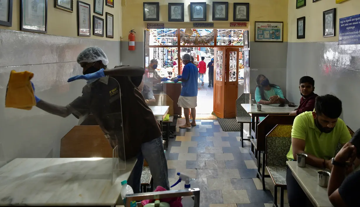 Pekerja membersihkan panel transparan yang membagi meja di restoran yang dibuka kembali usai pelonggaran lockdown di Bangalore, India, Senin (8/6/2020). Untuk keamanan pelanggan, restoran-restoran menyiapkan panel transparan sebagai bagian dari rangkaian pencegahan COVID-19. (Manjunath Kiran/AFP)
