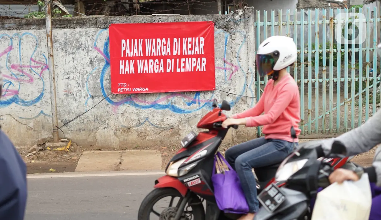 Pengendara motor melintas di depan poster protes warga terhadap pembangunan flyover di kawasan Tanjung Barat, Jakarta, Rabu (15/7/2020). Dalam poster protes tersebut, warga menuntut agar pembayaran pelunasan pembebasan lahan segera diselesaikan secara serentak. (Liputan6.com/Immanuel Antonius)