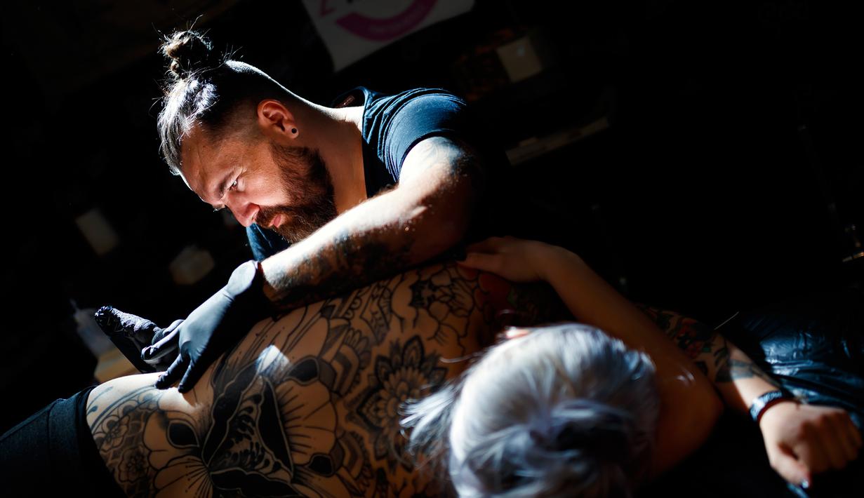 Seorang seniman  mentato badan pengunjung wanita dalam acara edisi keempat Montreux Tattoo Convention di Montreux, Swiss  (22/9). Montreux Tattoo Convention berlangsung selama tiga hari. (Valentin Flauraud/Keystone via AP)