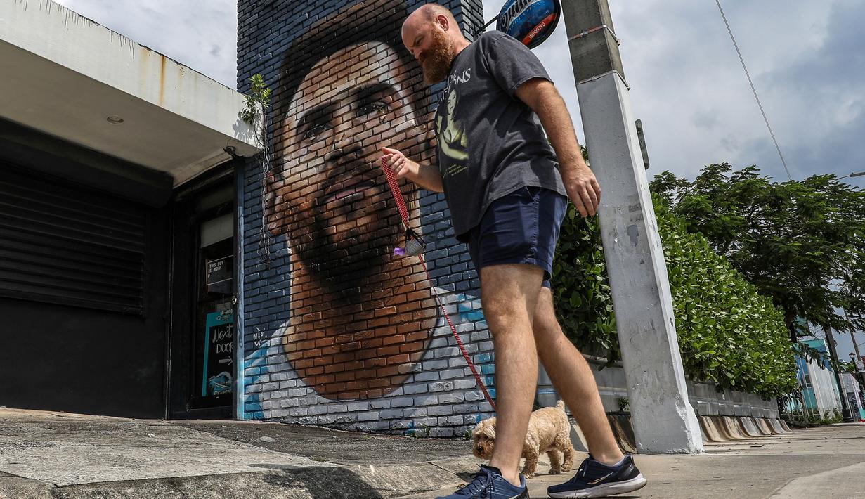 Pejalan kaki melintasi mural wajah Lionel Messi yang berada di salah satu jalan di Miami, Amerika Serikat. Messi memutuskan untuk bergabung dengan klub MLS, Inter Miami, pada Rabu (7/6/2023). (AFP/Giorgio Viera)
