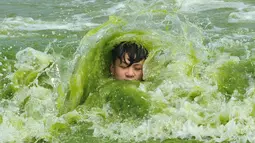 Seorang anak berenang di pantai yang dipenuhi tanaman ganggang di Qingdao , Provinsi Shandong , China , (18/7). Ganggang yang berbahaya bisa mengeluarkan racun yang melukai manusia, ikan, kerang-kerangan beserta hewan laut lain, dan burung. (Reuters)
