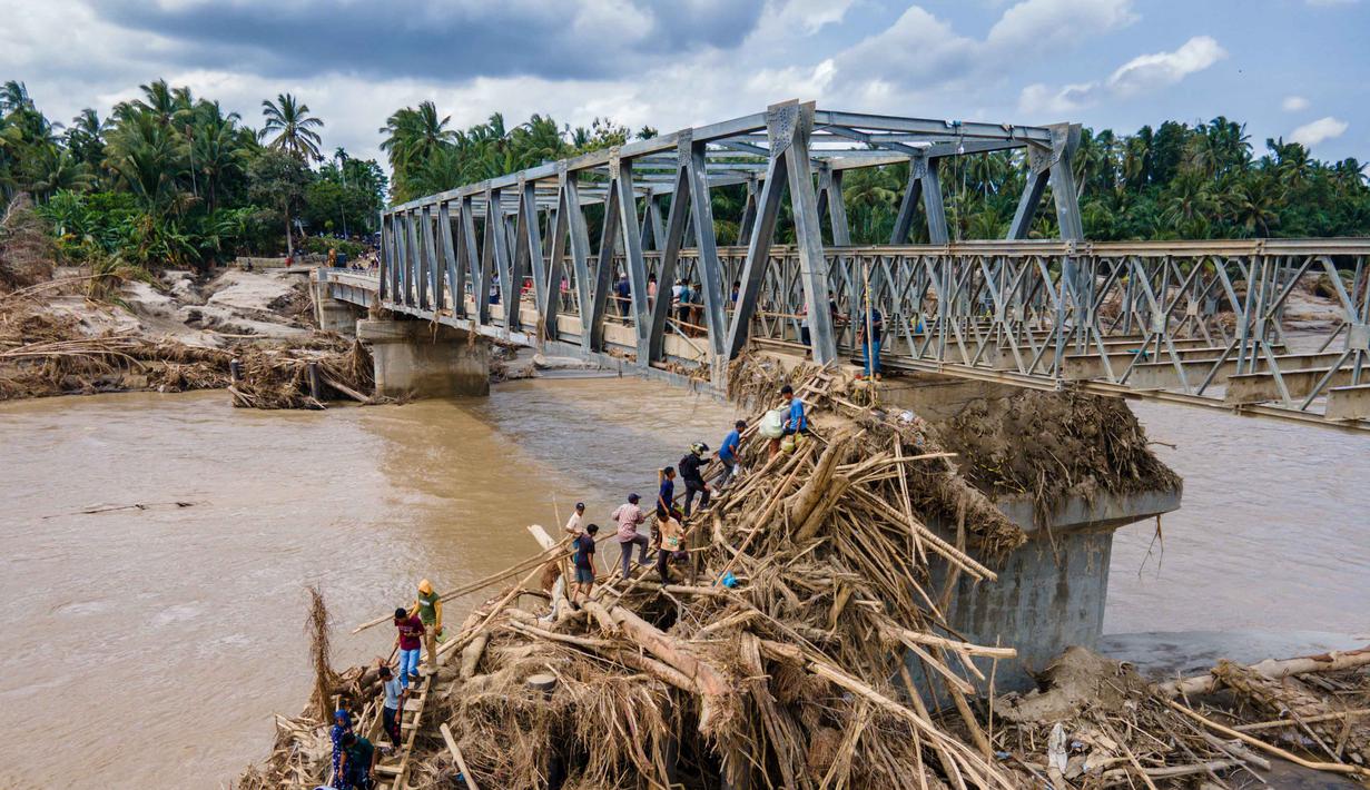 Diketahui, ada beberapa jembatan yang melintasi Sungai Peusangan di Kabupaten Bireuen, Aceh, dan dilaporkan putus atau rusak akibat banjir bandang pada akhir November 2025 lalu. Tampak foto udara menunjukkan warga memanjat puing-puing untuk menyeberangi sungai di jembatan yang baru dibangun yang menghubungkan Aceh dan Provinsi Sumatera Utara setelah hancur akibat banjir bandang di Sungai Peusangan di Distrik Bireuen, Provinsi Aceh, pada Selasa 9 Desember 2025. (CHAIDEER MAHYUDDIN/AFP)