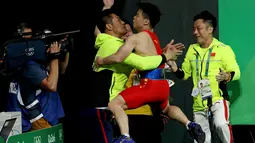 Atlet angkat besi putra China, Long Qingquan melakukan selebrasi dengan memeluk pelatihnya usai meraih kemenangan pada angkat besi 56kg putra di Olimpiade Rio 2016, Brasil (7/8). Long Qingquan meraih emas pada Olimpiade 2016. (REUTERS/Stoyan Nenov)