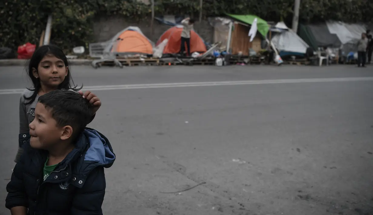 Anak-anak bermain di dekat tenda keluarga mereka yang didirikan di sebuah jalan di luar kamp pengungsi Eleonas di Athena (20/11/2019). Sekitar 14 pengungsi Afghanistan, termasuk keluarga dengan anak-anak, tinggal di luar kamp dalam tenda, tanpa fasilitas apa pun. (AFP/Louisa Gouliamaki)