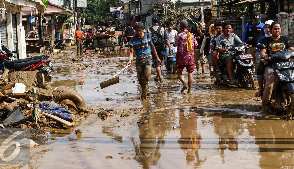 Warga dan pengendara motor melintas di sepanjang jalan yang dipenuhi lumpur di komplek Pondok Gede Permai Jatiasih, Bekasi, Jumat (22/04).Banjir yang telah merendam ratusan rumah warga mengakibatkan air lumpur mengendap. (Liputan6.com/Fery Pradolo)
