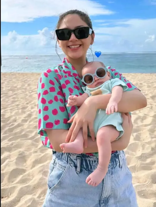 <p>Jessica Mila terlihat chic bahkan saat menggendong sang anak di pantai. Ia tampil kasual mengenakan kaus bercorak abstrak berwarna semarak dan celana jeans. Kyarra, sang putri juga tampil gemas dengan baju bayi berwarna biru muda pastel, dipakaikan sunglasses kecil agar serasi dengan sang mama. [Foto: Instagram/jesicamila03]</p>