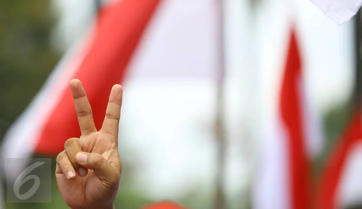 Pendukung Cagub DKI Basuki T Purnama memberikan salam dua jari saat sidang kasus penistaan agama, Jakarta, Selasa (10/1). Dengan mengenakan atribut kotak-kotak, massa membawa bendera Indonesia serta melakukan orasi damai. (Liputan6.com/Immanuel Antonius)