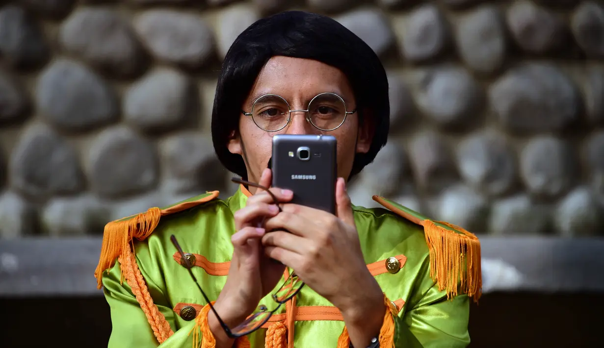 Seorang peserta mengambil gambar saat kegiatan untuk memecahkan rekor dunia dengan jumlah terbesar orang mengenakan pakaian dan bergaya seperti  The Beatles di sebuah taman di Mexico City, Meksiko 28 November 2015. (AFP PHOTO/ALFREDO ESTRELLA)