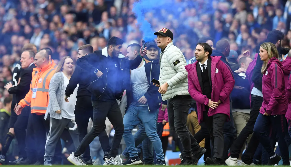 Fans menyalakan smoke bomb saat turun ke lapangan usai laga Manchester City melawan Swansea City pada lanjutan Premier League di Etihad Stadium, Manchester, (22/4/2018). Manchester City menang 5-0. (AFP/Paul Ellis)