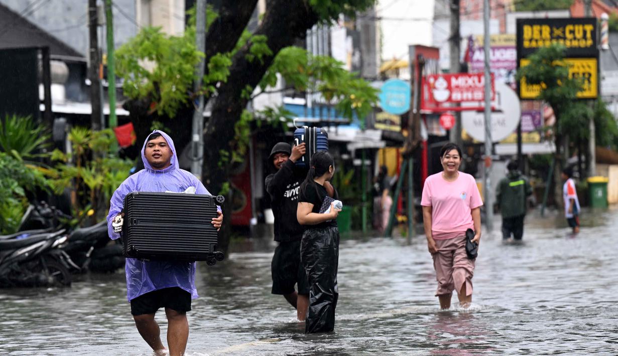 Banjir juga merendam ratusan rumah warga di sejumlah wilayah Bali. Tampak dalam foto, Para tamu hotel membawa koper mereka sambil menerobos air di jalan yang tergenang banjir akibat hujan lebat di Legian Kuta, Denpasar, Bali, pada Selasa 24 Februari 2026. (SONNY TUMBELAKA/AFP)