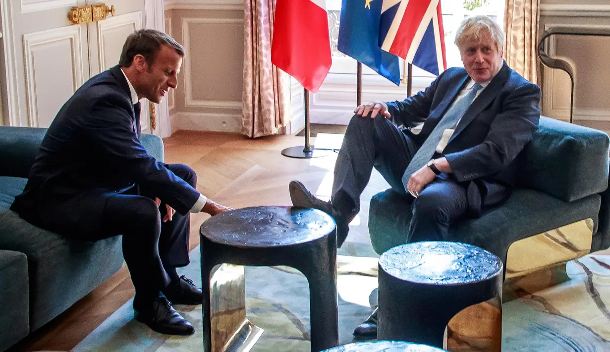 PM Inggris, Boris Johnson menaruh kaki di atas meja di depan Presiden Prancis Emmanuel Macron dalam kunjungan kenegaraan di Istana Elysee, Paris, Kamis (22/8/2019). Awak media mengabadikan momen ketika Johnson menumpangkan kakinya di meja kopi. (Christophe Petit Tesson, Pool via AP)