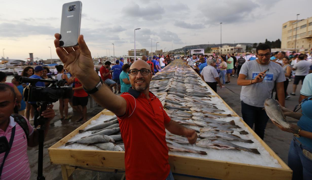 Seorang pria berfoto dengan latar belakang sejumlah ikan yang berhasil memecahkan rekor makanan laut terbanyak di daerah kota pantai Batroun, Minggu (4/9). Menurut panitia, total ikan yang dikumpulnya sebanyak 2 ton 614 kg. (AFP PHOTO/Anwar AMRO)