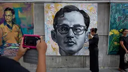 Seorang warga mengambil memotret lukisan mendiang Raja Thailand Bhumibol Adulyadej di luar Grand Palace, Bangkok, Thailand (13/10). Raja Bhumibol Adulyadej meninggal pada 13 Oktober 2016, di usia 88 tahun. (AP Photo/Gemunu Amarasinghe)