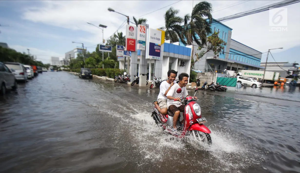 Dua orang remaja mengendarai motor melintasi banjir rob di kawasan Muara Baru, Jakarta, Rabu (6/11). Banjir Rob akibat laut pasang ini, membuat sejumlah aktivitas warga terganggu. Termasuk aktivitas di pasar ikan terhenti. (Liputan6.com/Faizal Fanani)