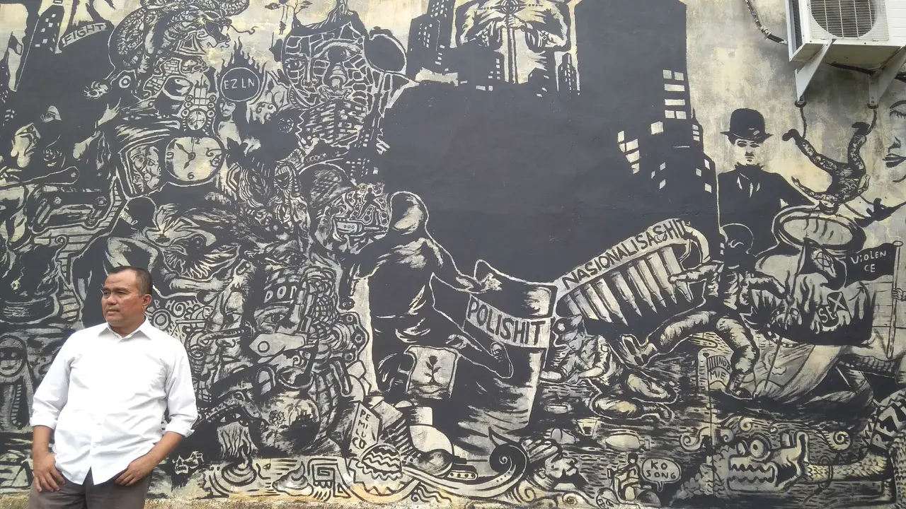 Saiful Mahdi berfoto dengan latar mural berjudul "Riots" (Liputan6.com/Rino Abonita)