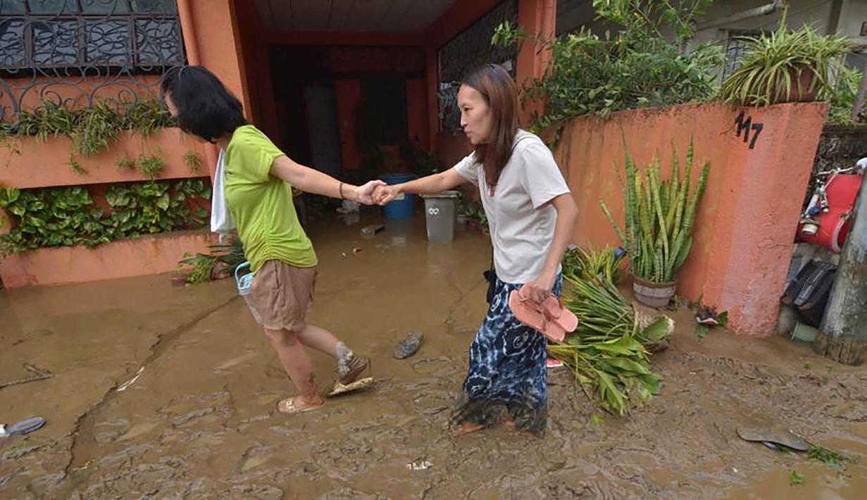 Warga berjalan di jalanan berlumpur setelah banjir akibat hujan deras yang dibawa Topan Kalmaegi di sebuah permukiman di Kota Cebu, Filipina tengah, pada Selasa 4 November 2025. Sedikitnya dua orang tewas, serta ribuan warga lainnya mengungsi ke tempat yang lebih aman. (Alan TANGCAWAN/AFP)