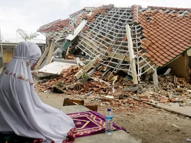 Seorang wanita berdoa di depan puing-puing bangunan di Lombok Barat, Nusa Tenggara Barat (NTB), Sabtu (11/8). BNPB menyatakan gempa Lombok hingga saat ini telah menewaskan 387 orang. (AP Photo/ Firdia Lisnawati)