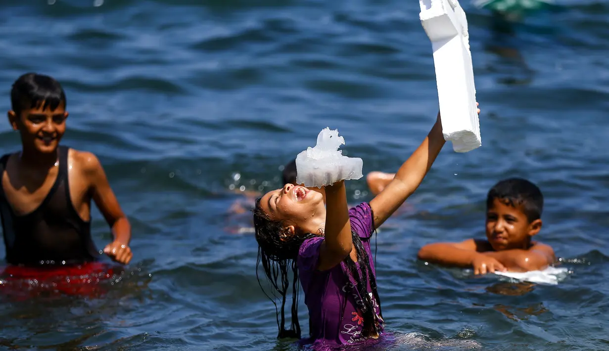 Seorang gadis Palestina tertawa sambil memegang ubur-ubur saat bermain bersama teman-temanya di laut Mediterania dekat kamp pengungsi al-Shati di Kota Gaza (3/7). (AFP Photo/Mohammed Abed)