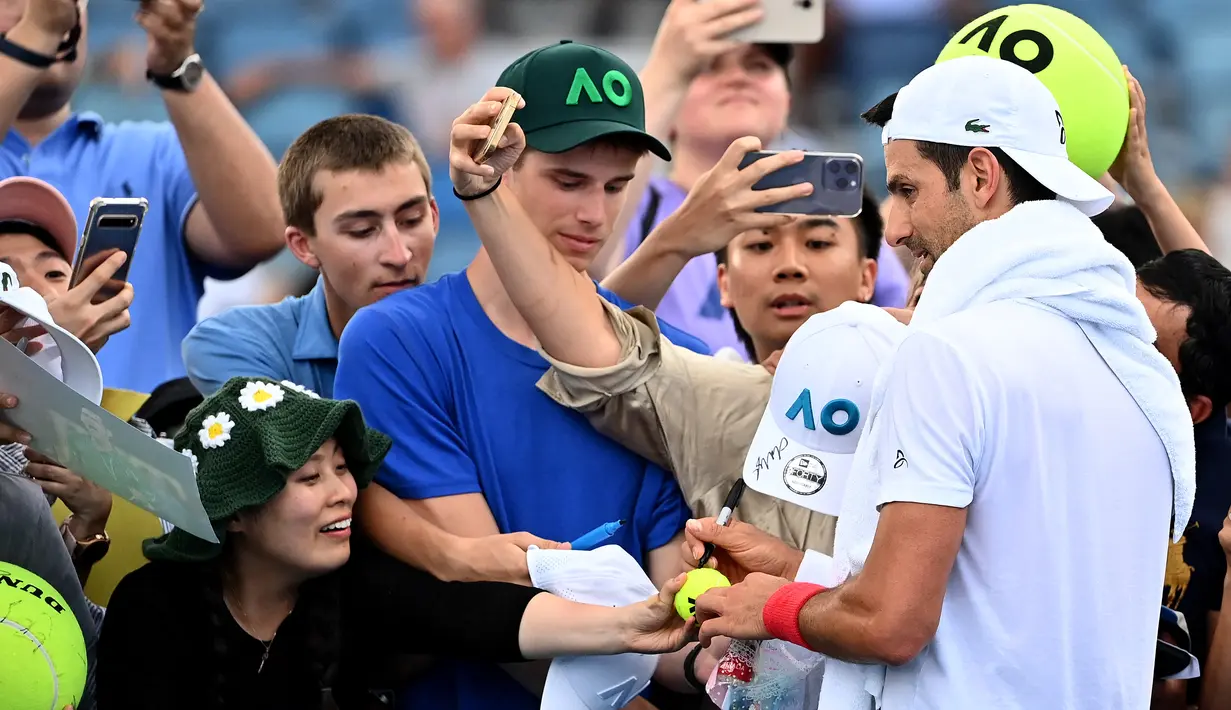 Petenis asal Serbia Novak Djokovic memberikan tanda tangan kepada para penggemar setelah sesi latihan pada hari kedua turnamen tenis Australia Terbuka di Melbourne pada 17 Januari 2023. Macam-macam barang pun disodorkan penggemar ke petenis pujaan. (MANAN VATSYAYANA / AFP)