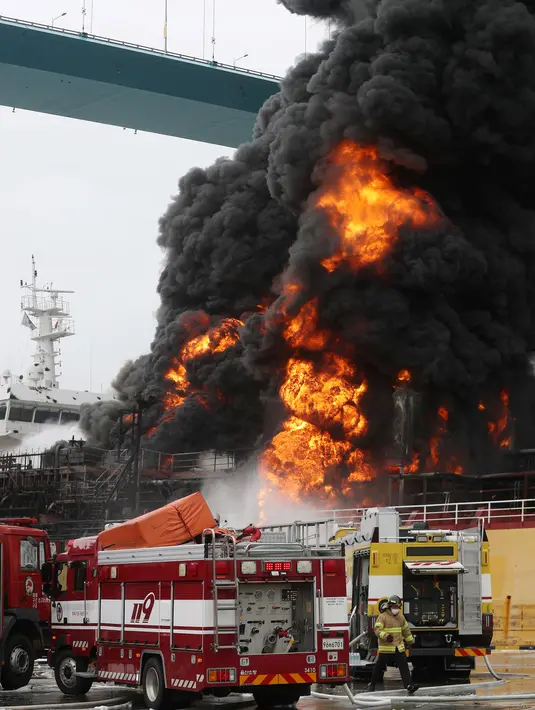 Petugas pemadam kebakaran menyeprotkan air ke arah kapal kargo yang terbakar di pelabuhan Ulsan, di pantai tenggara Korea Selatan (28/9/2019). Menurut pihak berwenang, sembilan pelaut terluka setelah kebakaran terjadi di kapal kargo dan menyebar ke kapal lainnya. (AFP/Yonhap)