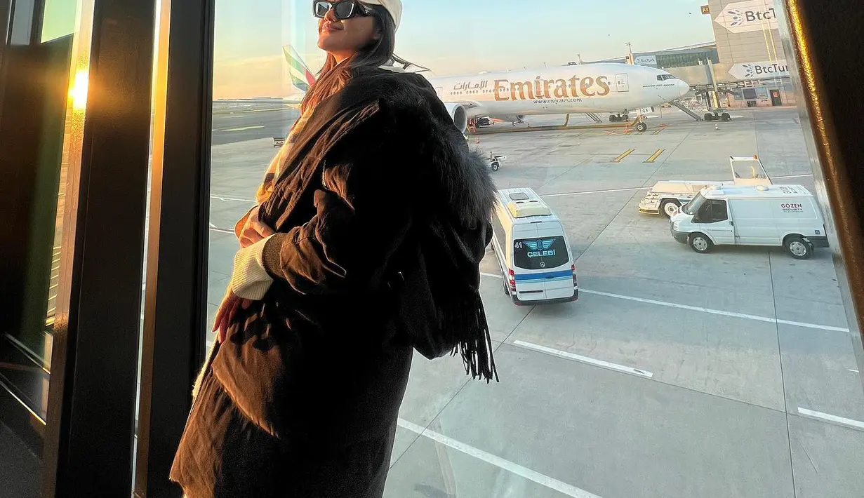 Gaya airport Camelia Putri yang sporty dan trendi. Dengan trench coat dan aksesori topi. [Foto: @cameliaputricp]