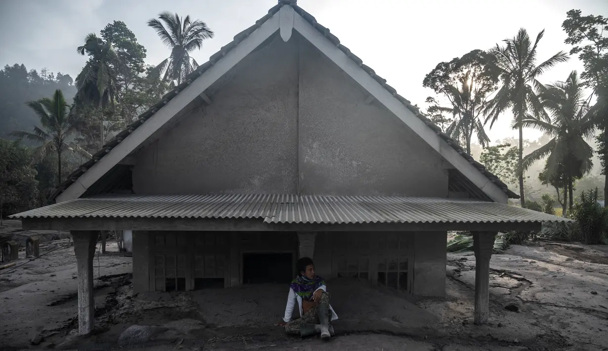 Seorang pria duduk di depan sebuah rumah yang terendam lumpur setelah letusan gunung berapi oleh Gunung Semeru di desa Kajar Kuning di Lumajang (5/12/2022). Gunung Semeru meletus pada tanggal 4 Desember memuntahkan awan abu panas setinggi satu mil dan sungai lava di sisinya sambil memicu evakuasi hampir 2.000 orang tepat satu tahun setelah letusan besar terakhirnya menewaskan puluhan orang. (AFP/Juni Kriswanto)