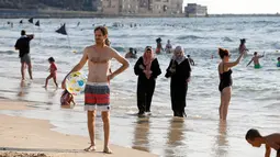 Dua orang wanita berjilbab berjalan di tepi pantai Laut Mediterania, Tel Aviv, Israel (30/8). Para wanita hijab ini tetap santai di tengah keramaian wanita berbikini. (REUTERS / Baz Ratner)