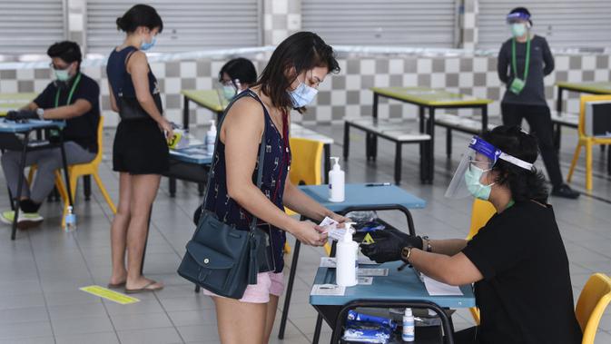 Pemilih mengenakan masker saat memverifikasi identitas dengan petugas pemilu di TPS Sekolah Tinggi Chung Cheng, Singapura, Jumat (10/7/2020). Pemilu di tengah pandemi COVID-19, warga Singapura memberikan suara mereka dengan mengenakan masker dan sarung tangan plastik. (AP Photo)