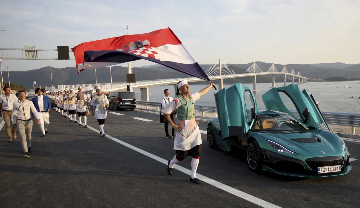 Seorang pria mengibarkan bendera Kroasia di sebelah mobil listrik 'Nevera' yang diparkir dekat Jembatan Peljesac yang baru dibangun di Komarna, Kroasia selatan, 26 Juli 2022. Kroasia menandai pembukaan kunci dan jembatan yang telah lama ditunggu-tunggu yang menghubungkan dua bagian dari garis pantai Laut Adriatik negara itu dengan melewati sebagian kecil wilayah Bosnia. (AP Photo)