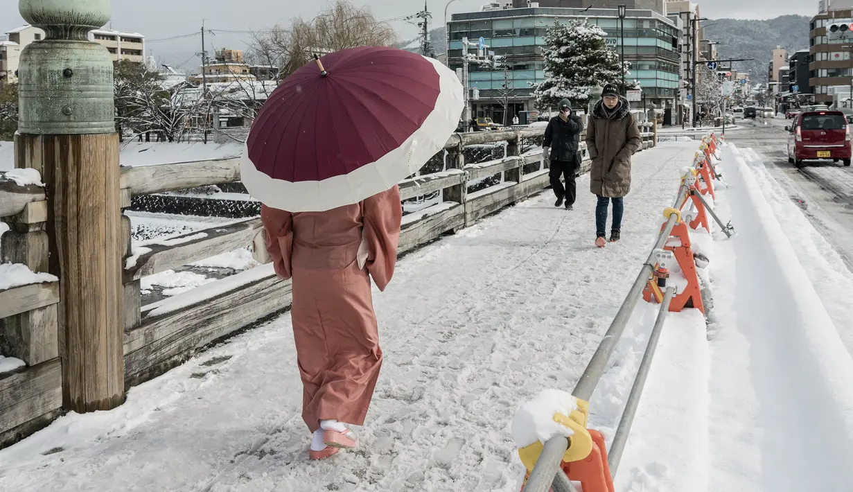 Pejalan kaki melintasi jembatan yang tertutup salju di atas Sungai Kamo setelah salju tebal dan angin kencang semalaman mempengaruhi wilayah luas negara itu di Kyoto, Jepang, Rabu (25/1/2023). Sejumlah area yang luas di Jepang, termasuk di sisi Pasifik, dapat mengalami hujan salju lebat dari Selasa malam 24 Januari 2023 hingga Rabu 25 Januari 2023. (Fred Mery / AFP)