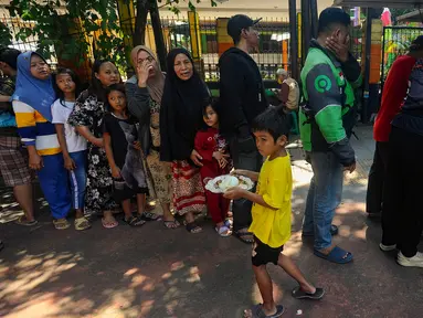 Warga antre mendapatkan sepiring nasi sayur dan lauk pauk saat pembagian makan siang gratis di wilayah Jati Padang, Pasar Minggu, Jakarta Selatan, Selasa (13/8/2024). (merdeka.com/Arie Basuki)