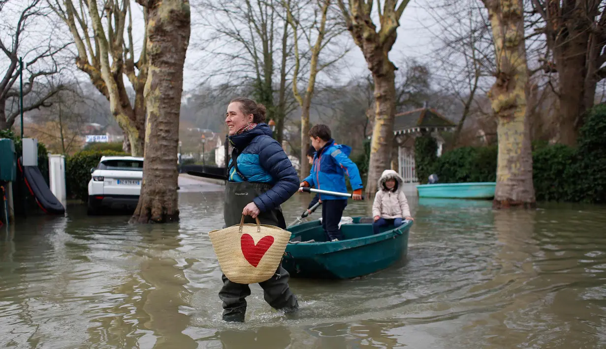 Seorang wanita menggunakan perahu membawa anak-anak di sebuah jalan banjir di Villennes sur Seine, sebelah barat Paris, (30/1). Sejumlah perjalanan kapal pesiar juga tergangu akibat hujan deras yang membuat sungai meluap. (AP Photo / Thibault Camus)