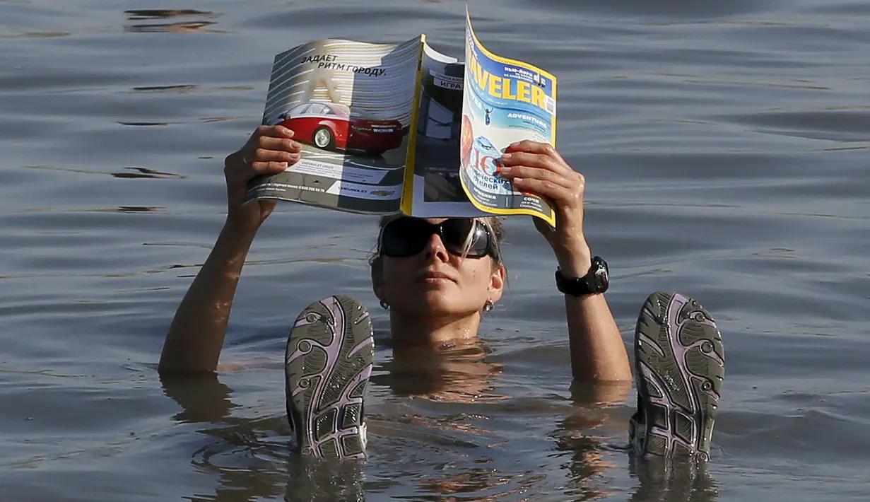 Seorang wisatawan wanita berendam sambil membaca majalah di Danau Tus, Khakassia, barat daya dari kota Siberia Krasnoyarsk, Rusia (18/7/2015). Selama musim panas, warga Rusia dari berbagai daerah melakukan perjalanan ke danau Tus. (REUTERS/Ilya Naymushin)