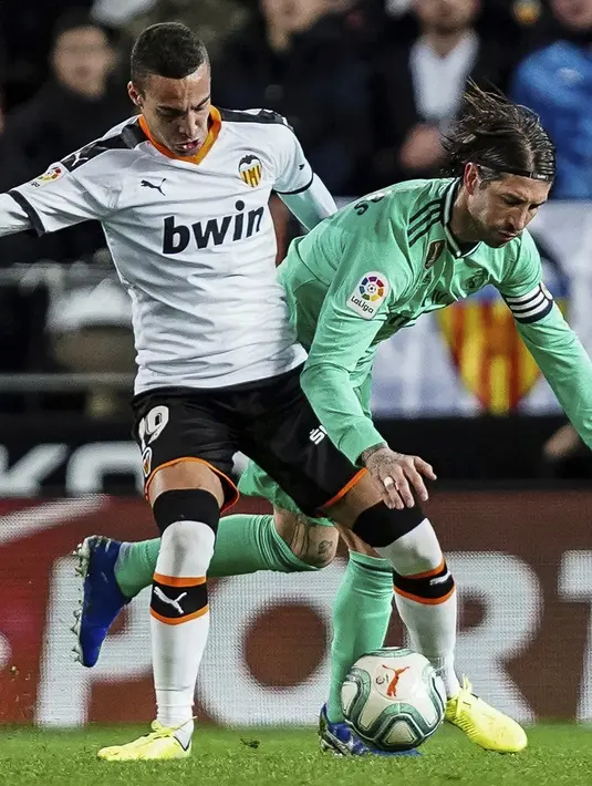 Penyerang Valencia, Rodrigo Moreno berebut bola dengan bek Real Madrid, Sergio Ramos pada pertandingan lanjutan La Liga Spanyol di Stadion Mestalla (15/12/2019). Madrid bermain imbang 1-1 atas Valencia. (AP Photo/Alberto Saiz)