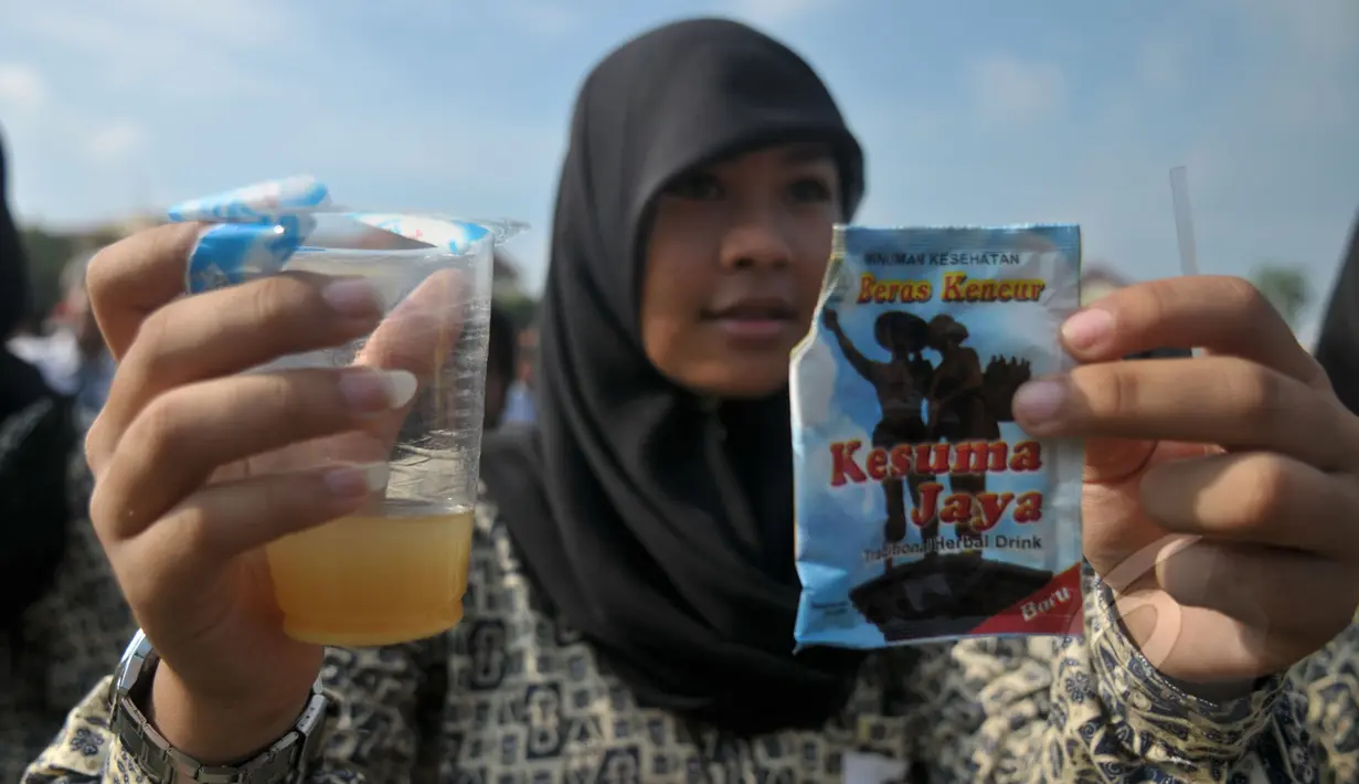 Seorang pelajar mengangkat gelasnya saat minum jamu bersama di Alun-Alun Satya Negara Sukoharjo, Jawa Tengah, Rabu (1/4/2015). Kegiatan tersebut dalam rangka pelestarian jamu ke masyarakat nasional maupun internasional. (Liputan6.com/Johan Tallo)