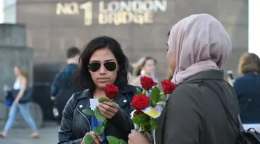 Mawar yang disertai sebuah pesan dibagikan kepada para pejalan kaki di London Bridge, Minggu (11/6). Muslim Inggris membagikan ratusan mawar sebagai bentuk solidaritas menyusul serangan teror London yang terjadi pekan lalu. (David Mirzoeff/PA via AP)