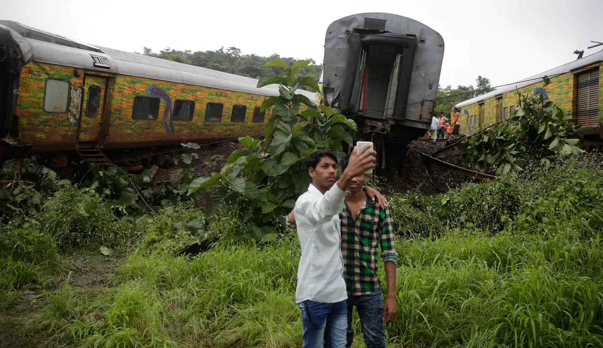 Dua remaja India berswafoto di dekat gerbon kereta yang tergelincir di Asangaon, India (29/8). Sebuah kereta penumpang mengalami kecelakaan di  sekitar 70 kilometer dari Mumbai. (AP Photo / Rafiq Maqbool)