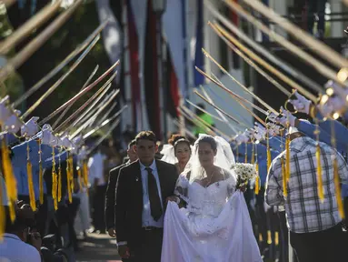 Pasangan berjalan di bawah penjaga kehormatan pedang kadet polisi saat pernikahan massal pada Hari Valentine di Managua, Nikaragua, Selasa (14/2/2023). Acara tersebut diselenggarakan oleh stasiun radio Sandinista "La Nueva Radio Ya", dan sekitar 263 pasangan menikah di Lapangan Revolusi. (AP Photo/Inti Ocon)
