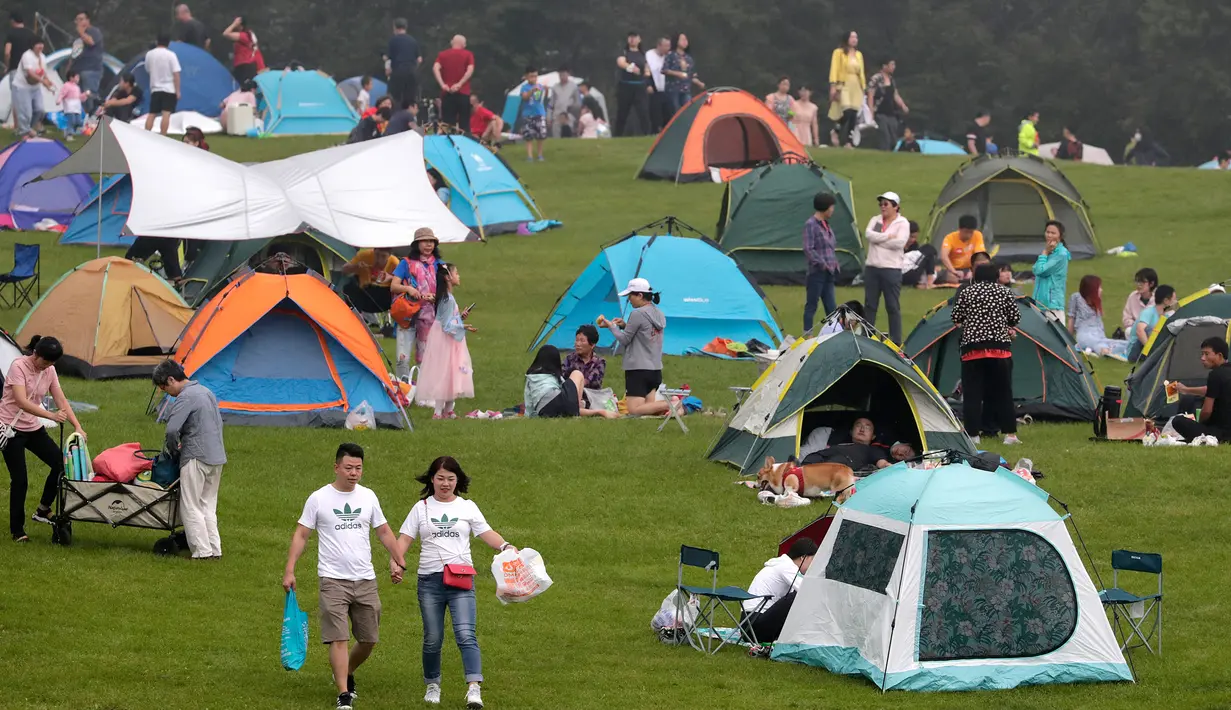 Sepasang suami istri melewati orang-orang yang berkemah di gunung yang indah di Yanqing, pinggiran Beijing, 30 Agustus 2020. China memiliki lebih dari 200 orang yang dirawat di RS karena COVID-19, dengan lebih dari 300 lainnya diisolasi usai dites positif terkena virus tanpa gejala. (AP/Andy Wong)